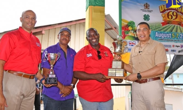 Prime Minister, the Most Hon. Andrew Holness (right), presents the 2023 National Champion Farmer trophy to Managing Director of Unity Boer Goat Farm, Owen Bartley (second right), during the recent staging of the 69th Denbigh Agricultural, Industrial and Food Show at the Denbigh Showground in Clarendon. Sharing the moment (from left) are Vice-President at Hi-Pro, Colonel (Ret’d) Jaimie Ogilvie and Managing Director of the Jamaica Social Investment Fund (JSIF), Omar Sweeney.  